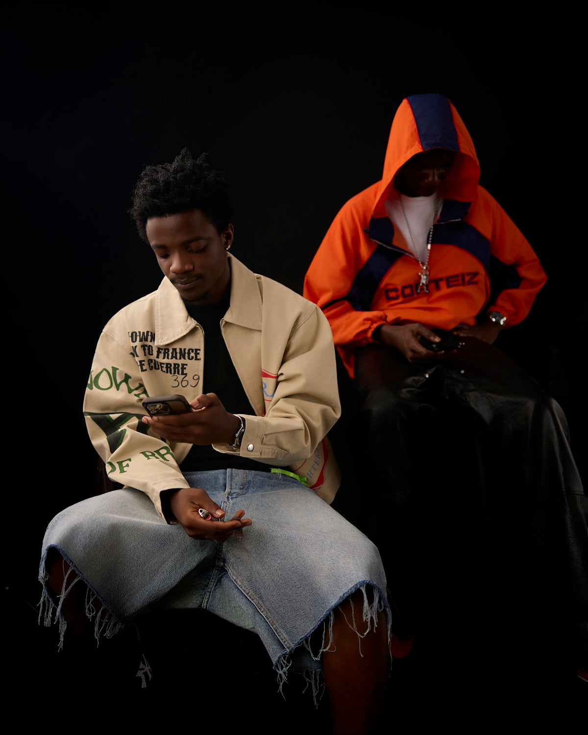 Two people in casual streetwear using smartphones against a plain black background